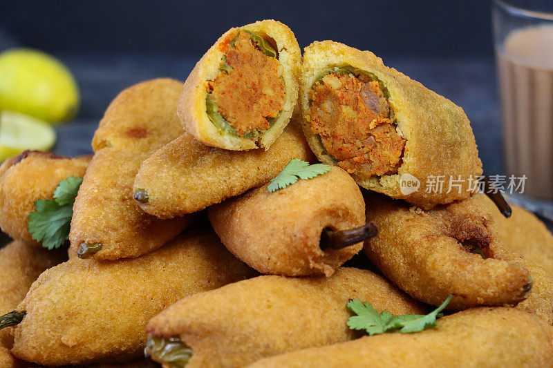 近距离的图片，堆熟的绿辣椒油炸饼(mirch pakora)，炸辣椒馅的aloo混合(土豆泥，洋葱和马沙拉)，印度街头小吃，一杯印度茶，不健康的饮食，灰色的背景，重点在前景